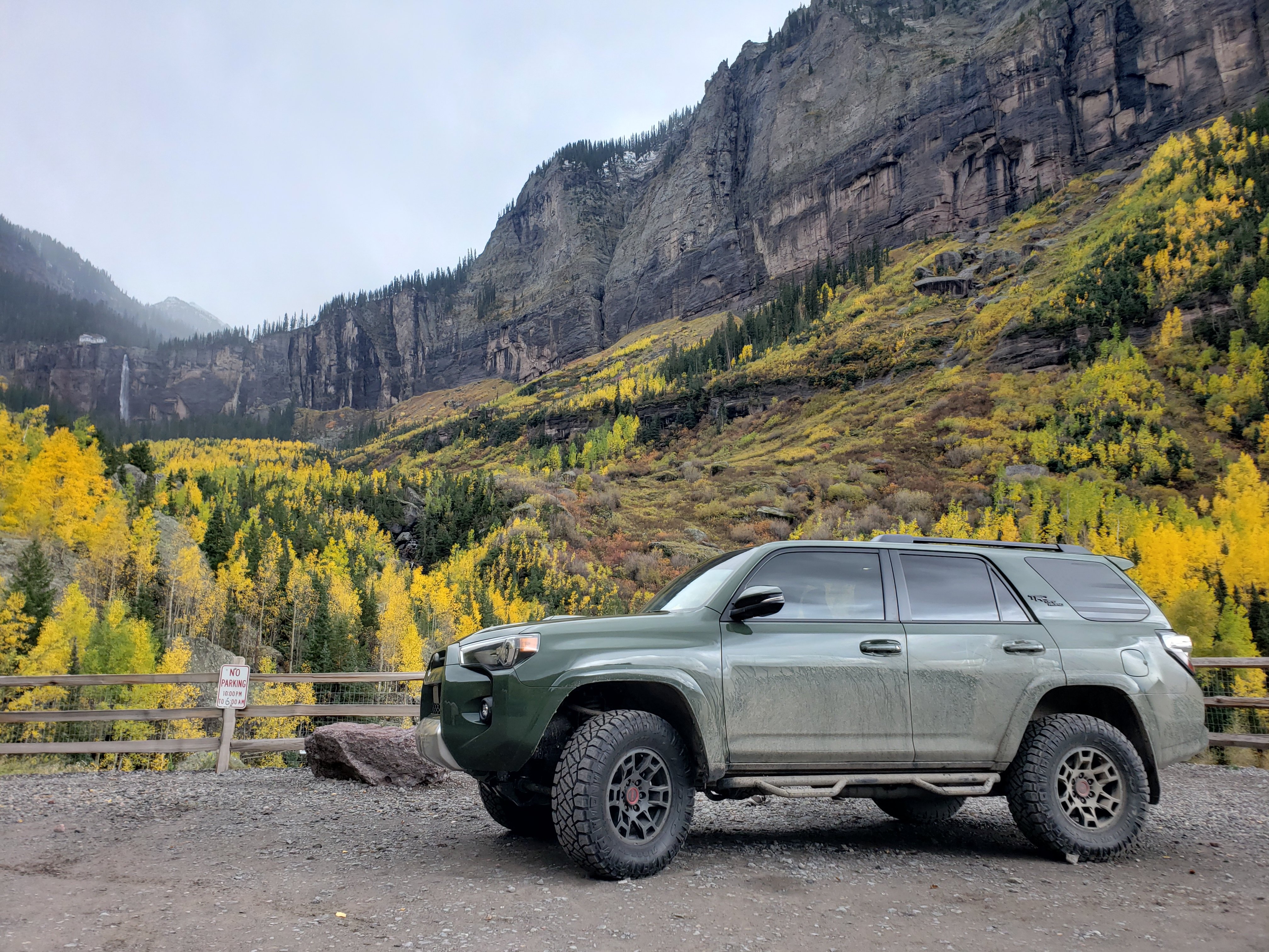 Green Toyota 4Runner with off-road tires and rock sliders parked in a mountain valley surrounded by rocky cliffs and autumn-colored trees.