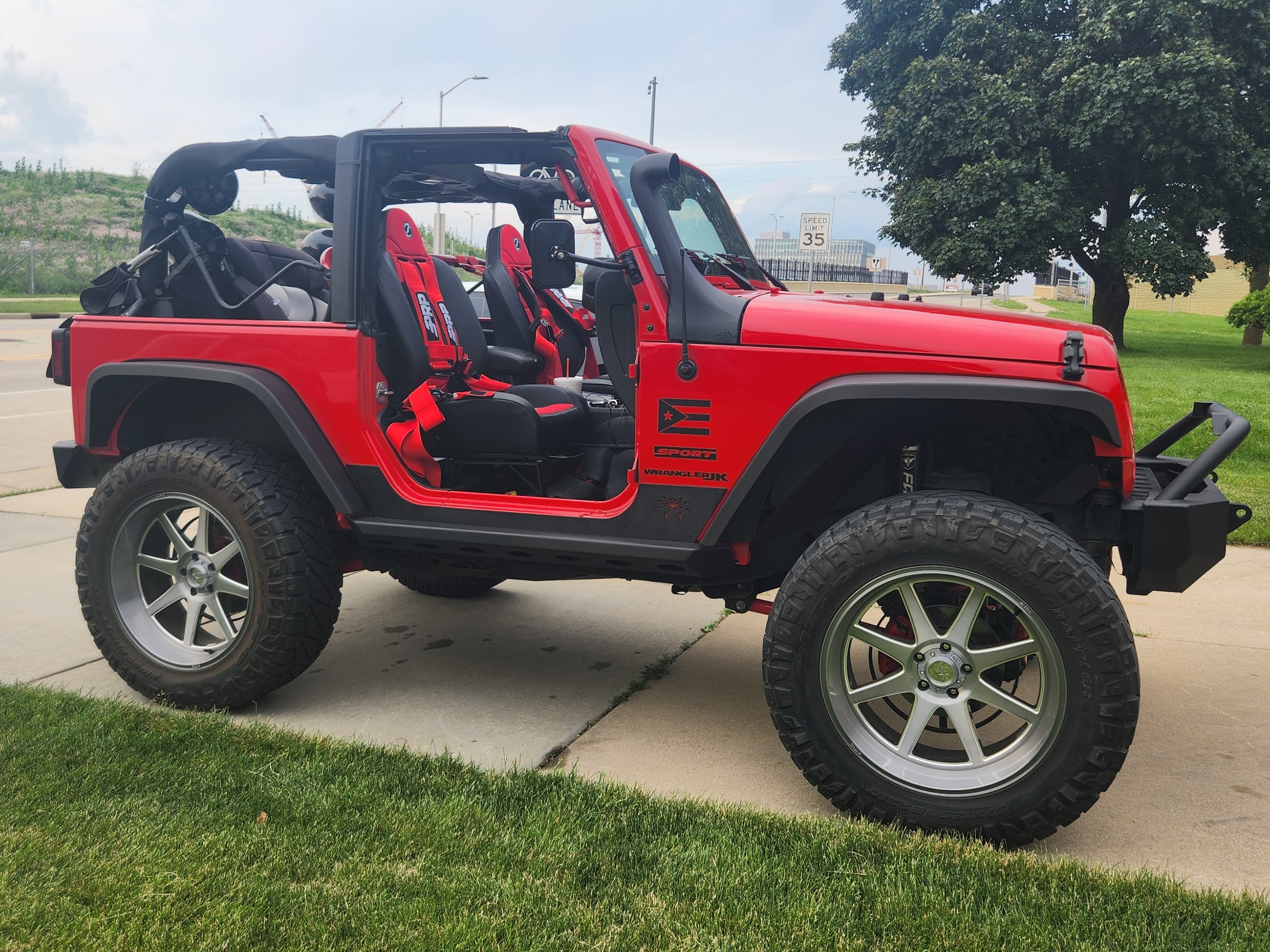 Red Jeep Wrangler equipped with off-road safety gear, including harness seats, roll bars, lifted suspension, and oversized all-terrain tires.