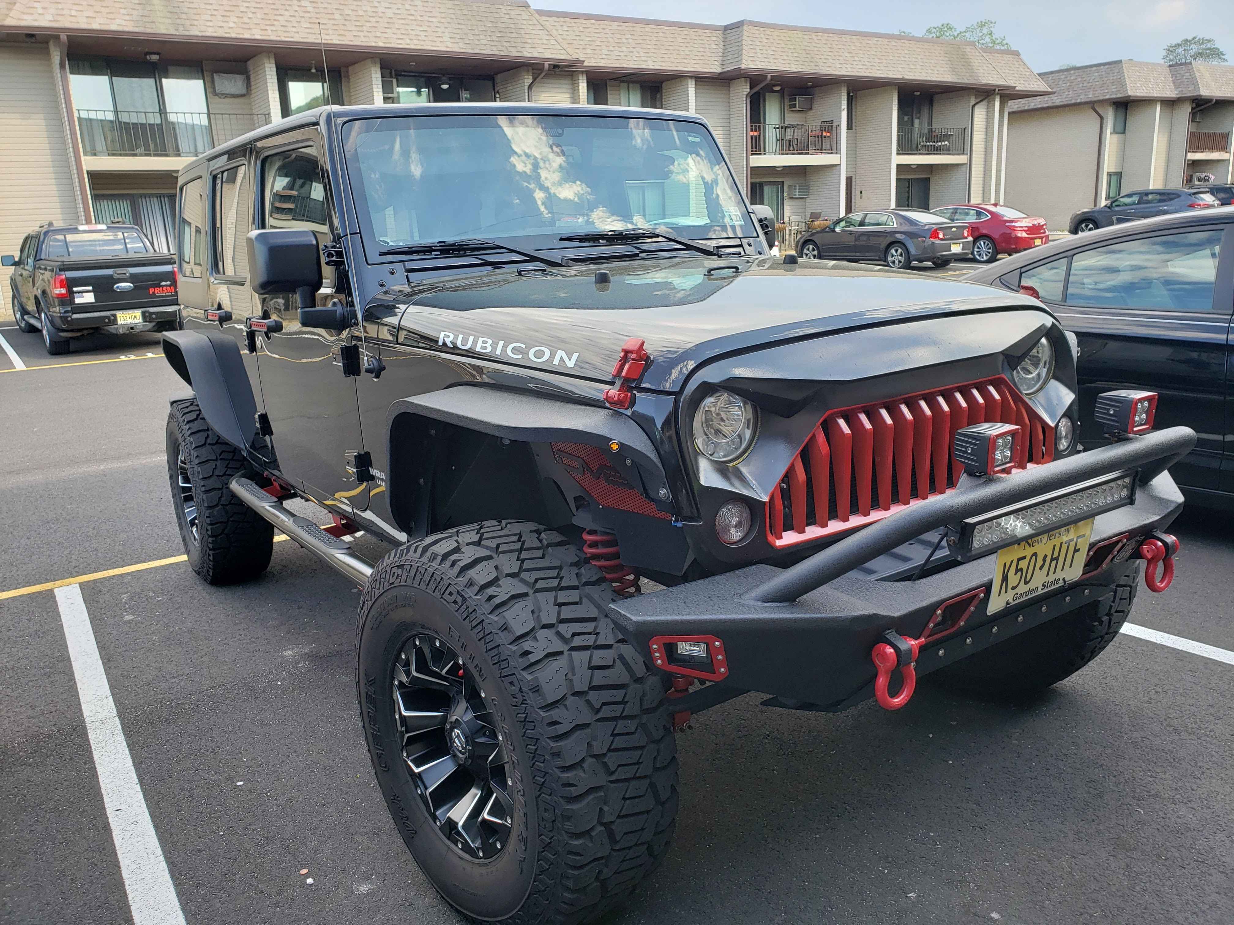 Black Jeep Wrangler Rubicon with oversized off-road tires, aftermarket front bumper, recovery shackles, auxiliary lights, and a skid plate installed beneath the front bumper for added trail protection.
