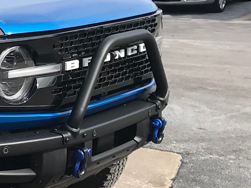 Close-up of a blue Ford Bronco front grille with a black bull bar bumper and blue recovery shackles.