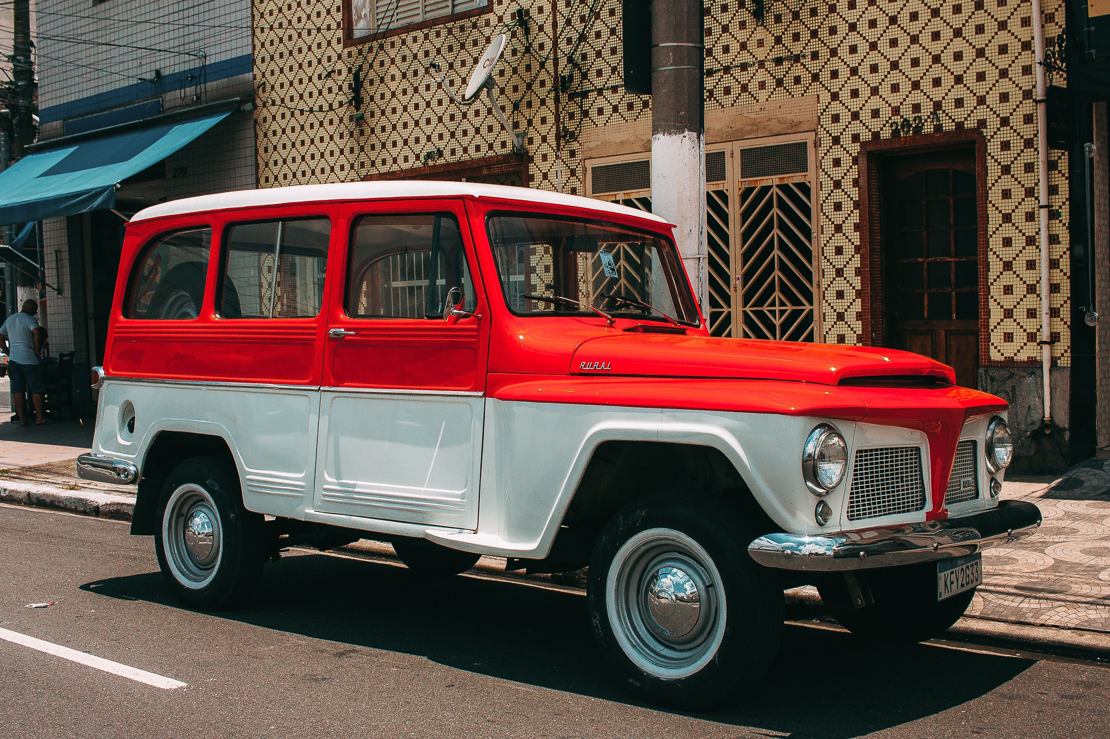 Vintage red-and-white Jeep Rural wagon parked on a city street, featuring classic boxy styling, chrome trim, and retro utility vehicle design.
