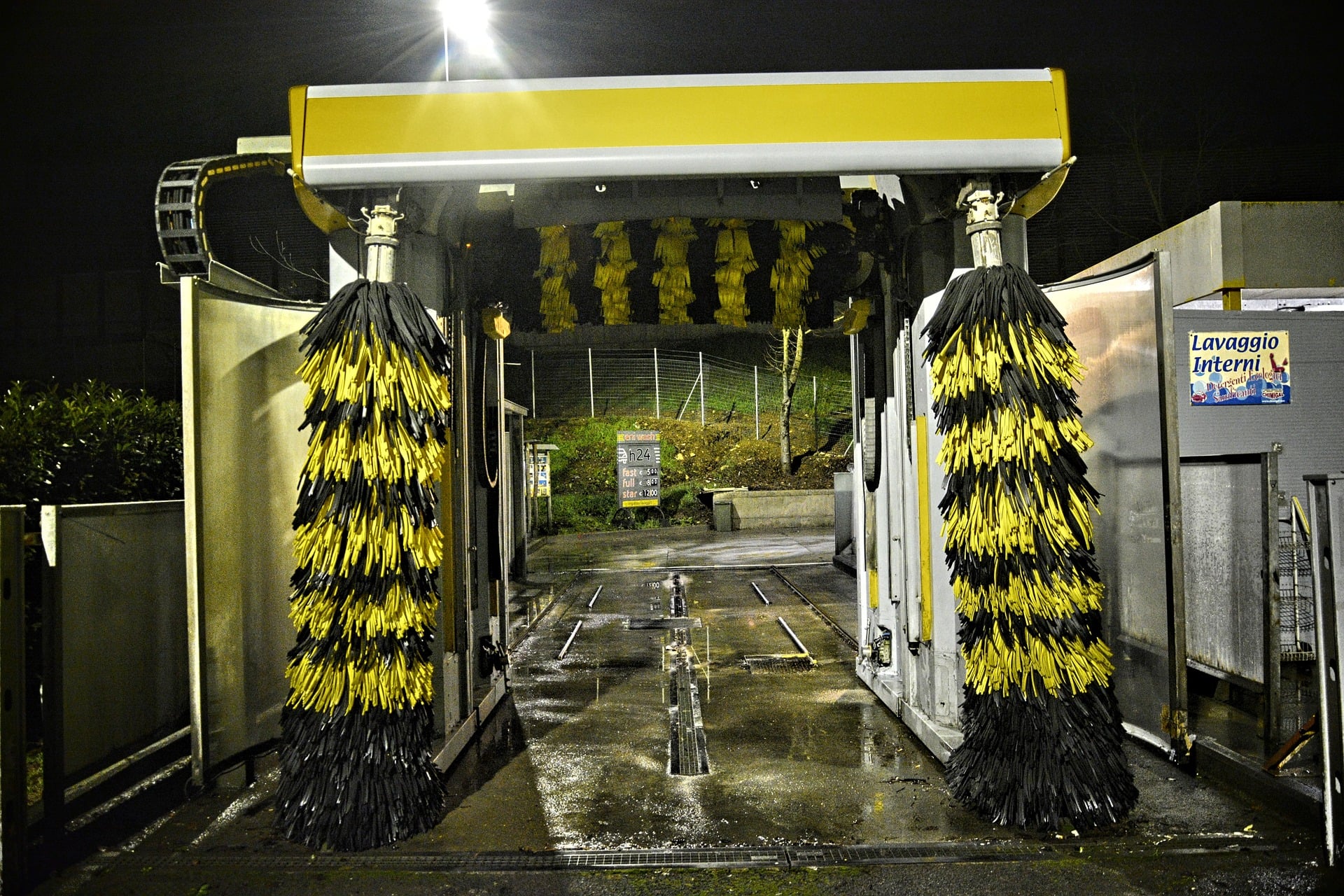 Touchless automatic car wash bay with large rotating black-and-yellow cleaning brushes, overhead wash equipment, and guide rails for vehicle alignment.