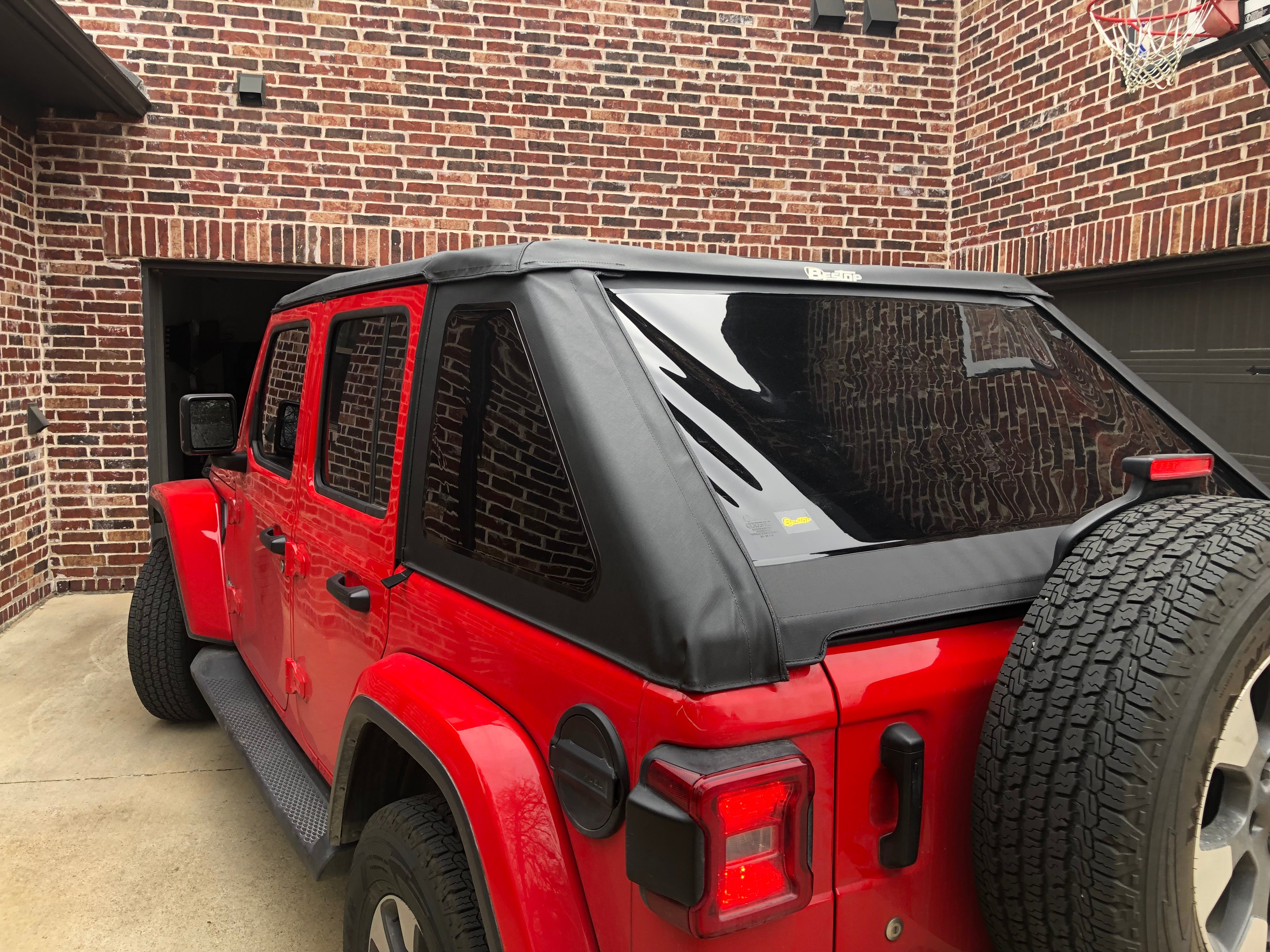 Red Jeep Wrangler Unlimited with a black soft top parked in a driveway, featuring tinted windows, full steel doors, side steps, and a rear-mounted spare tire.