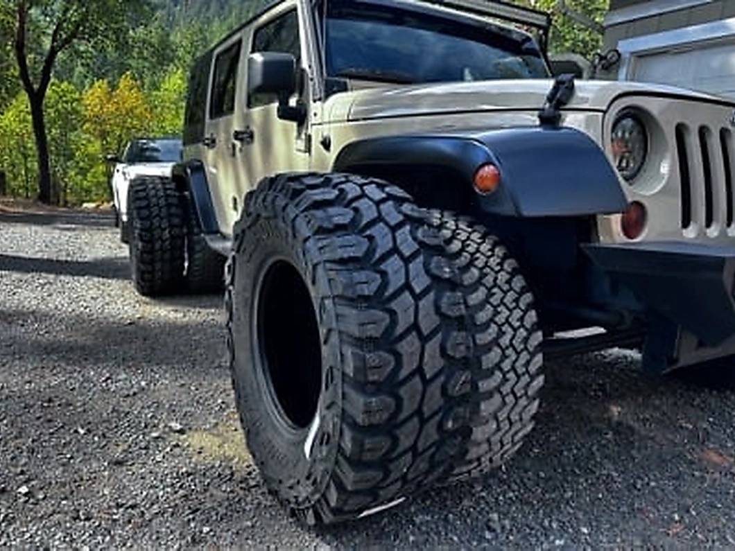 Large mud-terrain tire positioned next to a lifted Jeep Wrangler JK, highlighting the increased tire size commonly paired with lift kits.