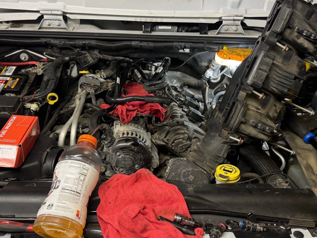 Engine bay with the intake manifold removed during a spark plug replacement, exposing the ignition system and cylinder heads for maintenance.