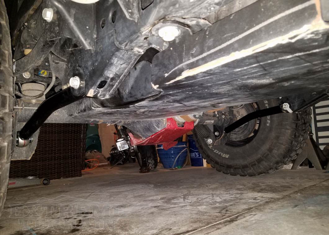 Aftermarket front control arms installed on the front suspension of a lifted Jeep Wrangler.