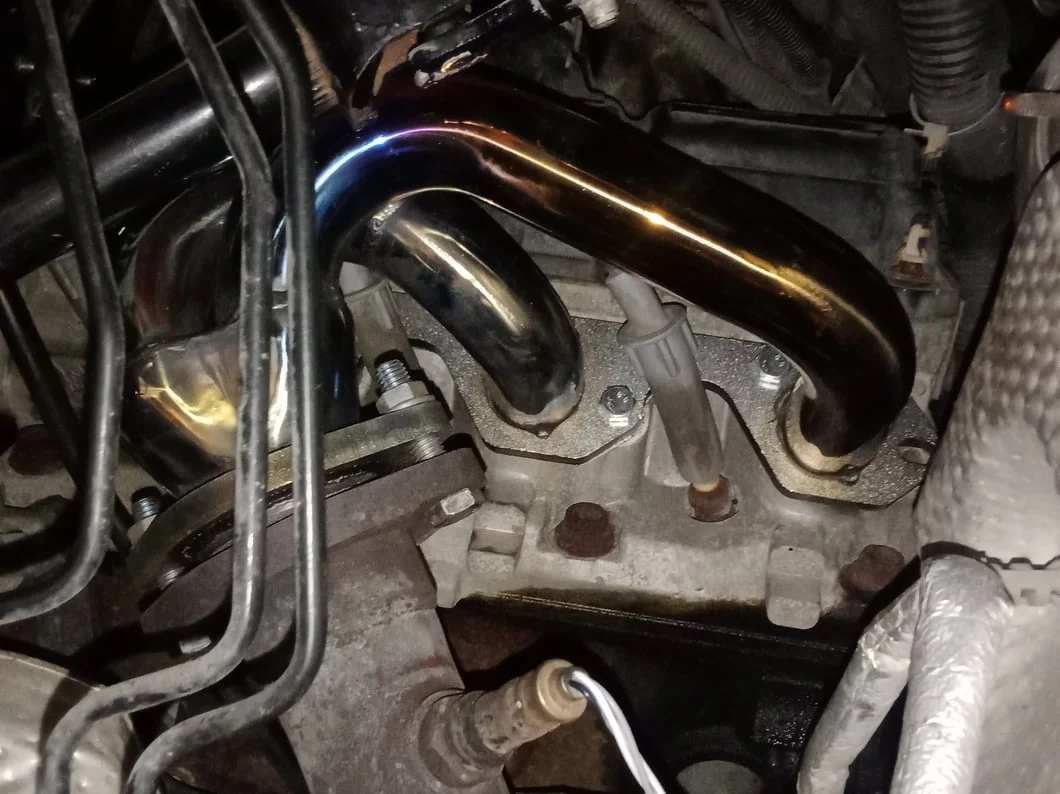 Aftermarket tubular exhaust header installed on a Jeep 4.0L inline-six engine.