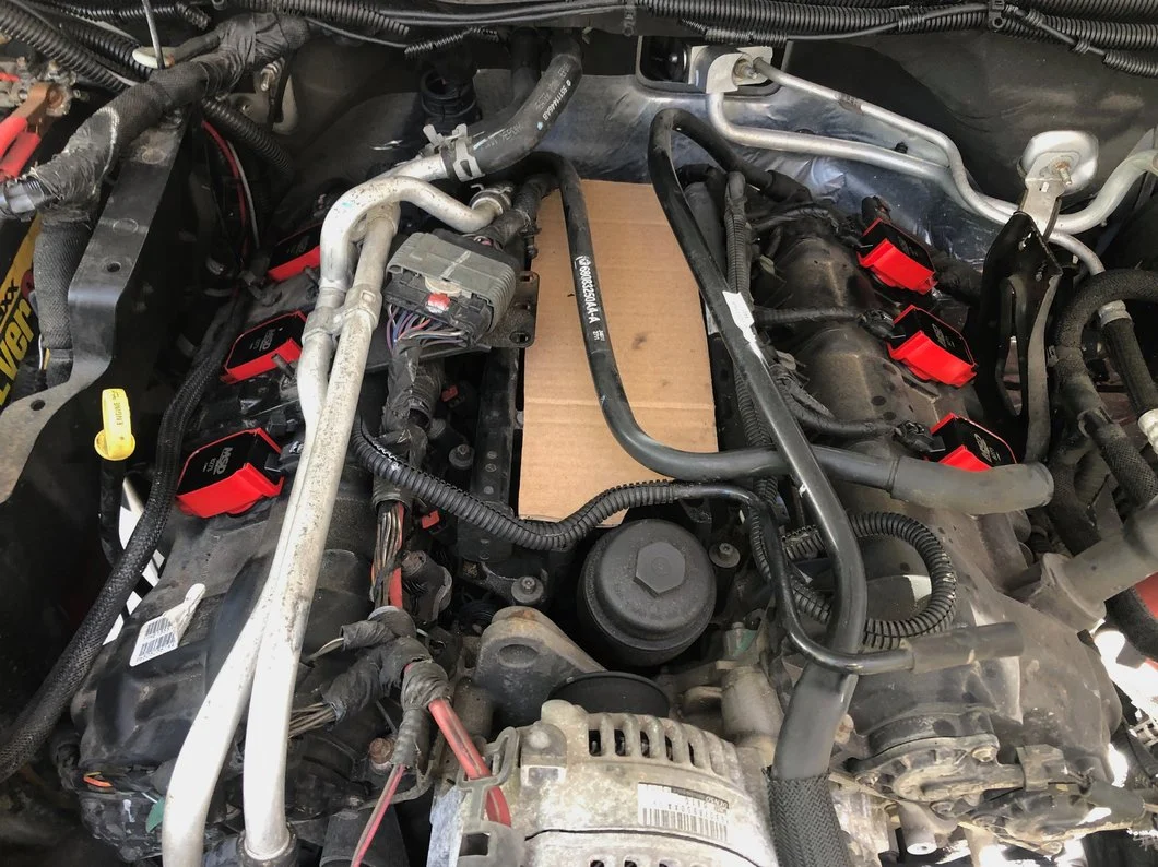 V8 engine bay with aftermarket ignition coils installed on both cylinder banks, showing upgraded coil packs and exposed valve covers during ignition system maintenance.